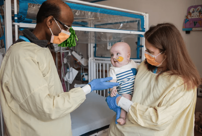 Doctors in gowns and masks stand with a baby.
