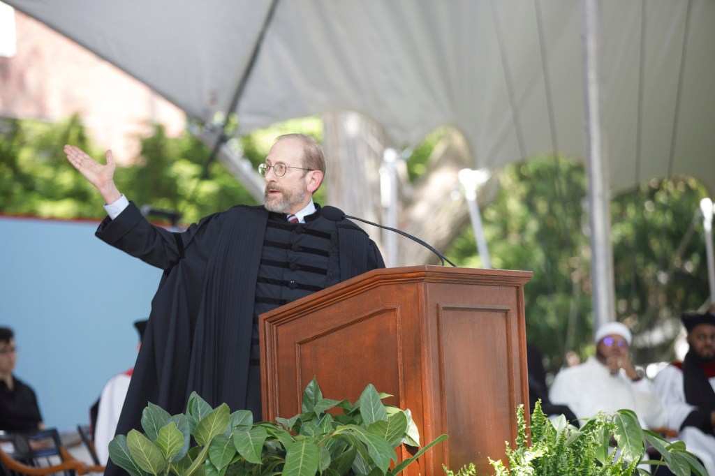 Alan Garber stands at a podium with his arm extended outward.