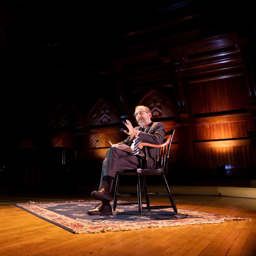 President Garber sitting in a spotlight on a dark stage, speaking to a crowd.