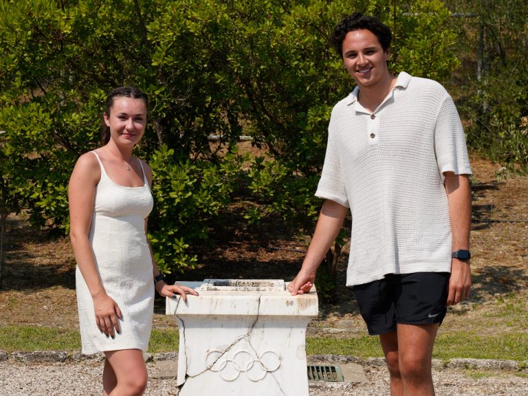 Two students standing next to a podium with Olympic rings carved into it
