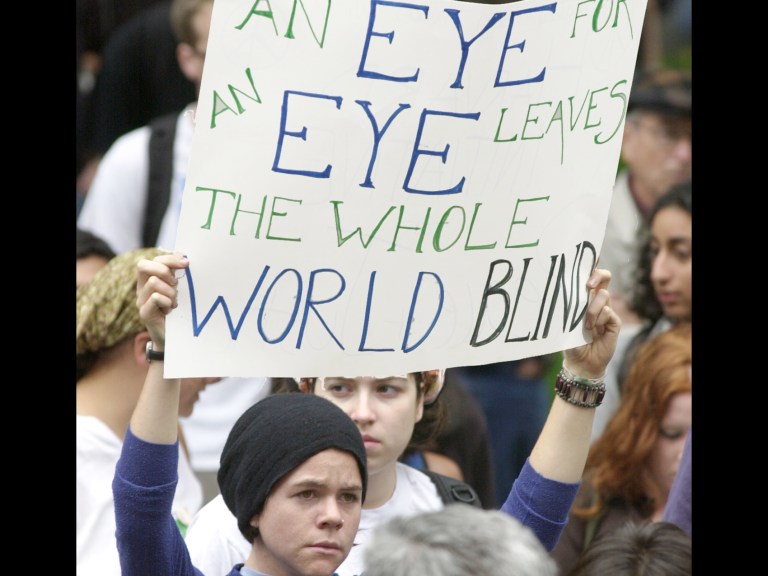 A woman holding a sign that says "An eye for an eye leaves the whole world blind"