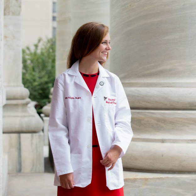 A medical school student wearing a white coat stands in front of a stone pillar