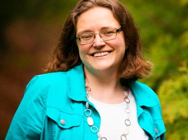 A woman stands outside by trees