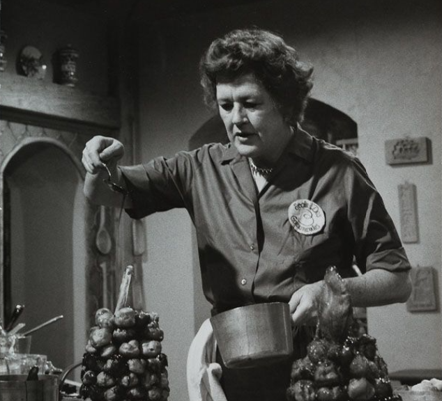 Julia Child pours hot syrup over a Croquembouche in a kitchen
