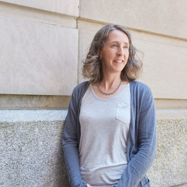 A woman stands outside, against a stone wall