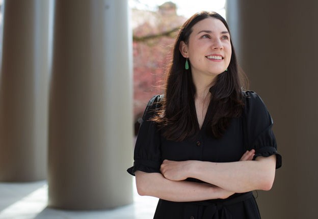 A woman with her arms crossed stands outside by stone pillars