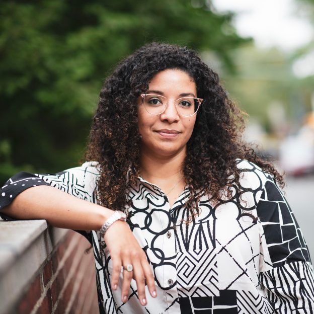 A woman stands outside, resting her arm on a brick wall