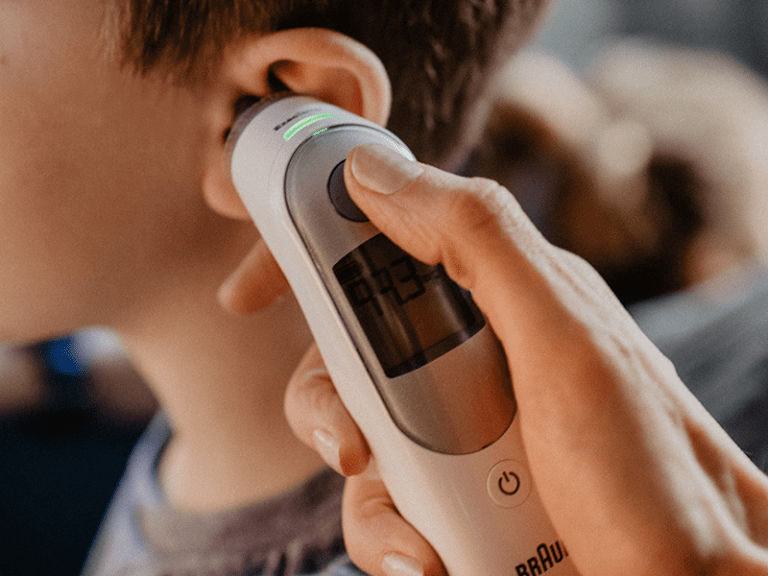 An adult takes a child's temperature using an ear thermometer