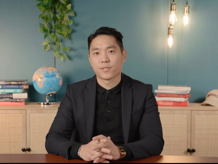 A man sits at a desk with a globe and plant behind him