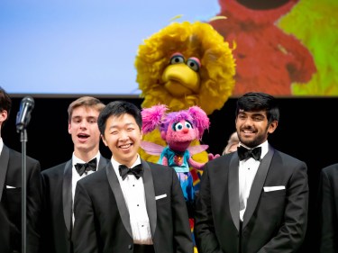 Big Bird, another muppet and Harvard students wearing tuxedos on stage