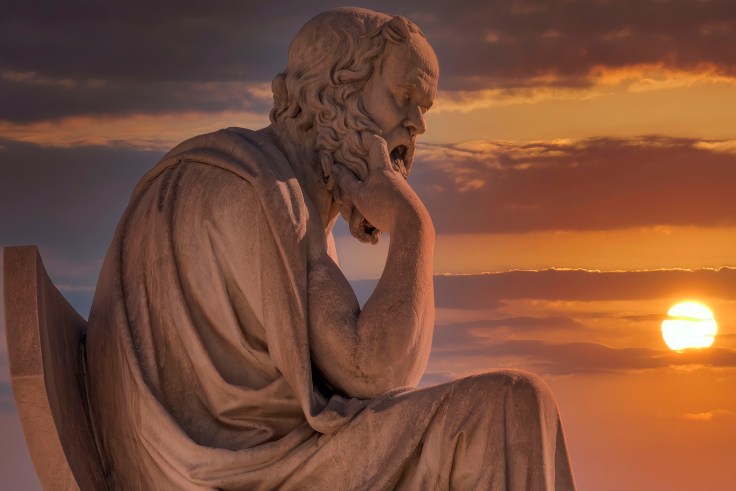 A statue of a philosopher in front of a sunset