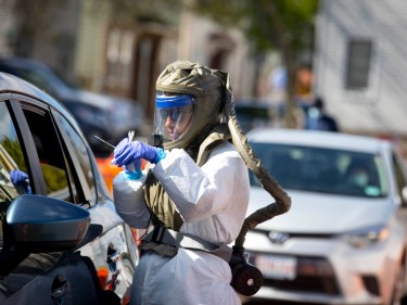 A person wears a full protective suit while assessing patients in a car