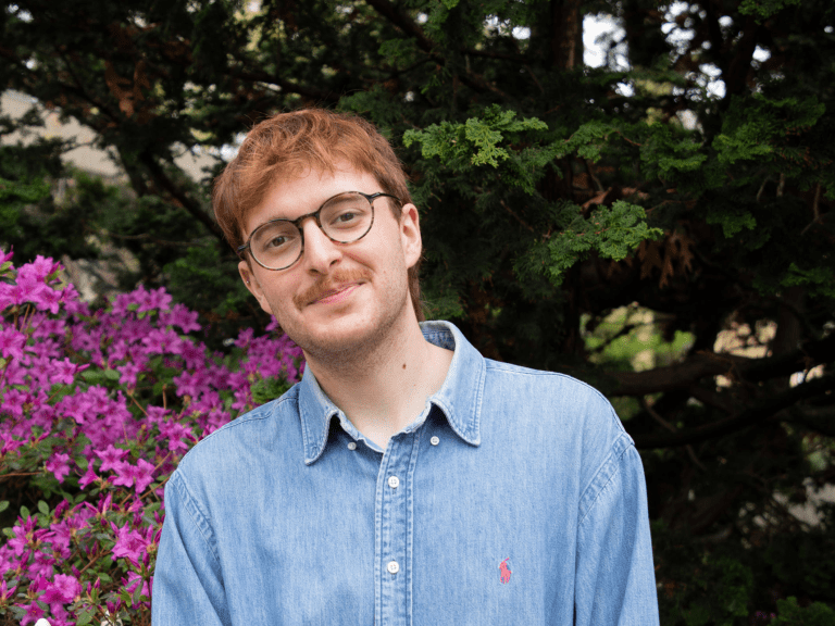 A young man poses in front of a bush with pink flowers