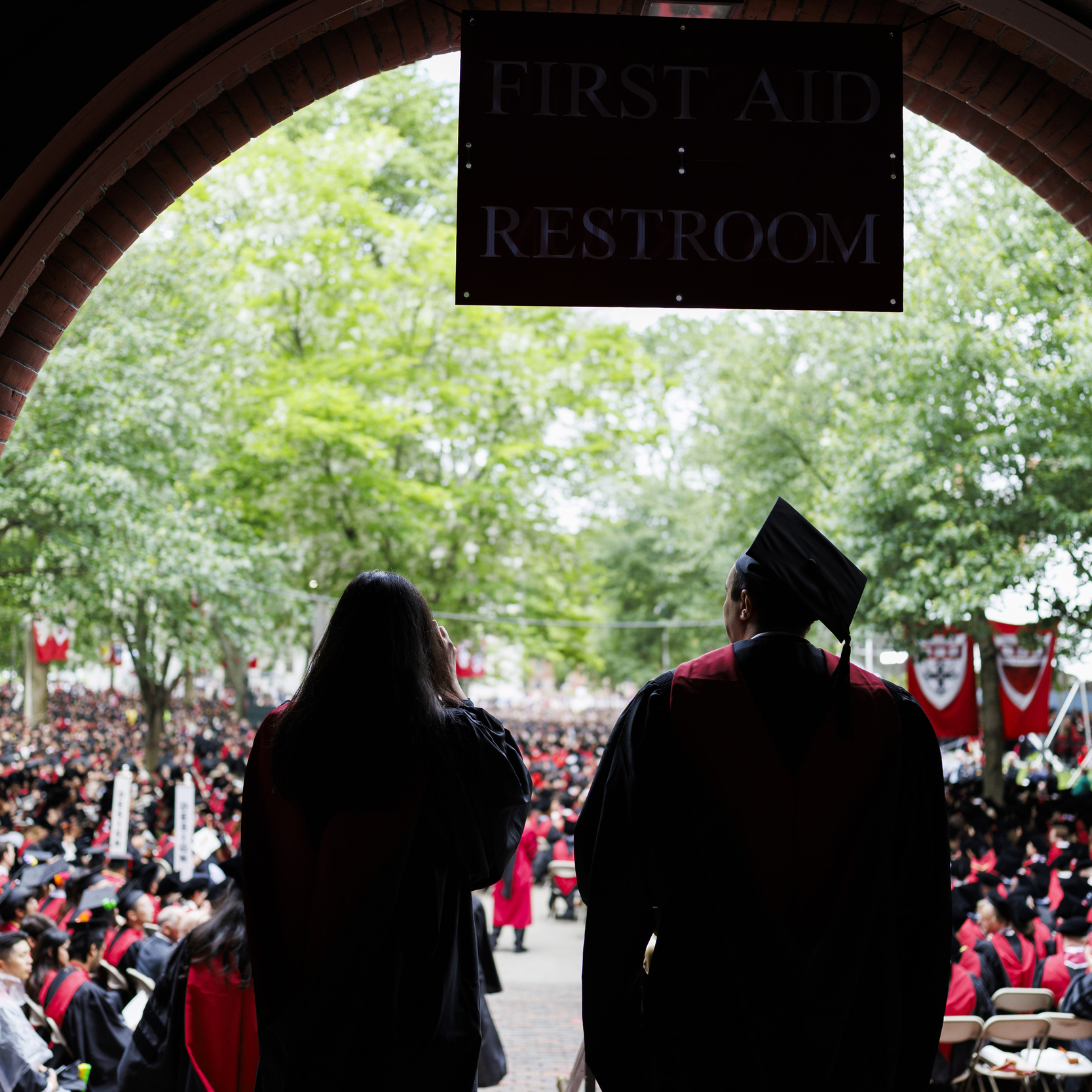 Silhouette of two graduates with the crowd seating before them.