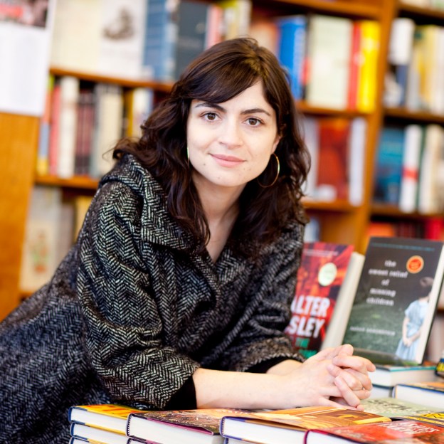 A woman leans over a table covered in books