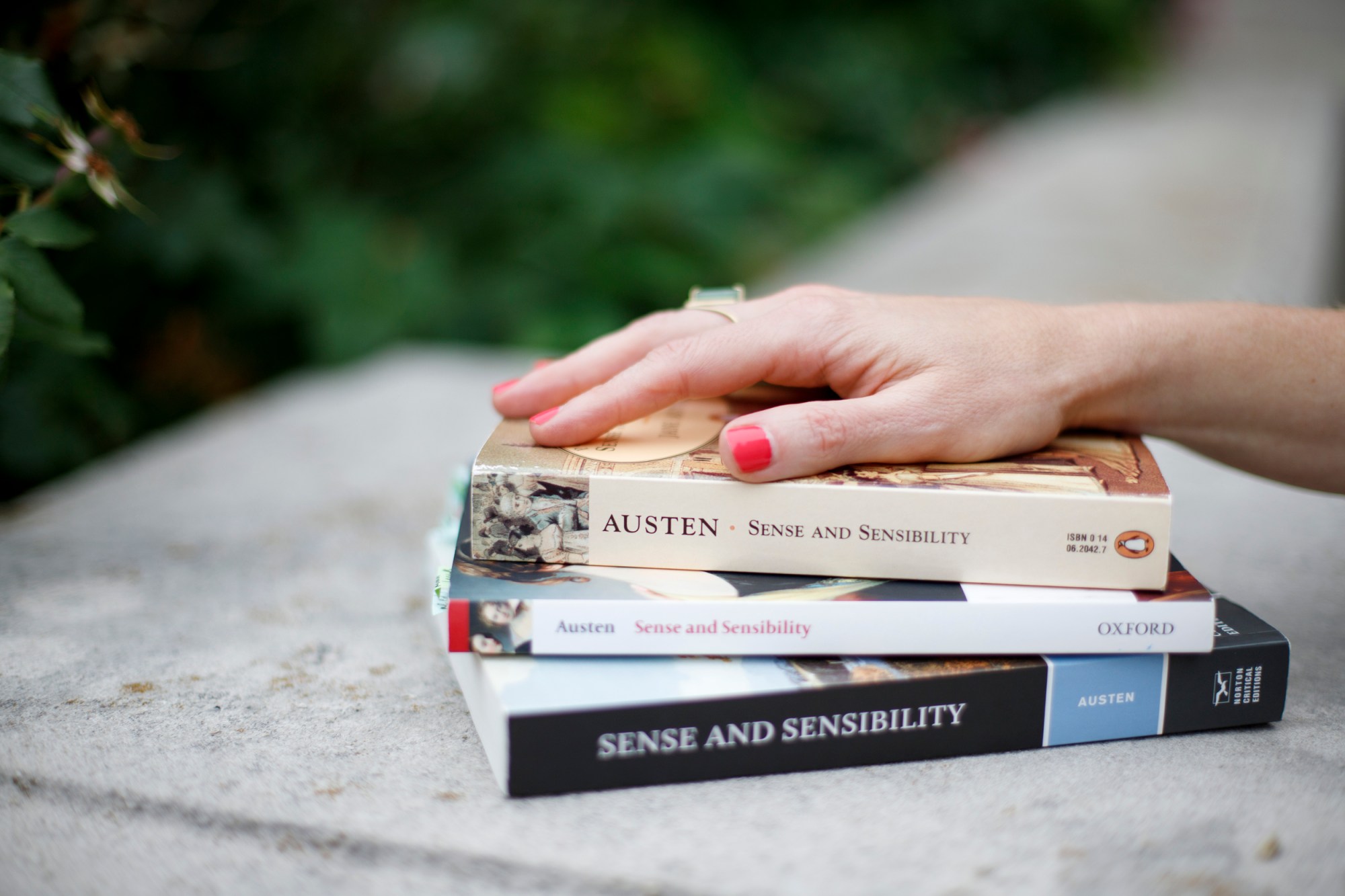 A woman's hand sits on top of three copies of "Sense and Sensibility" by Jane Austen