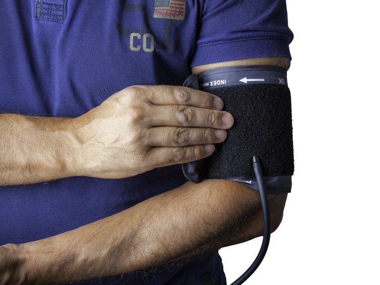 A man in a blue shirt holds a blood pressure cuff on his arm